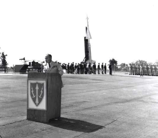 Ceremony marking activation of the first operational Nike-Hercules unit on the east coast at W-25 on Sept. 4, 1958. The firing unit is Battery B-1st Missile Battalion-562d Artillery. In the top photo, Army Vice Chief of Staff Lyman L. Lemnitzer delivers remarks at podium blazoned with ARADCOM insignia--yellow missile and lighting bolts on a red shield trimmed yellow. Note Nike-Ajax on launcher behind band in the background. 
